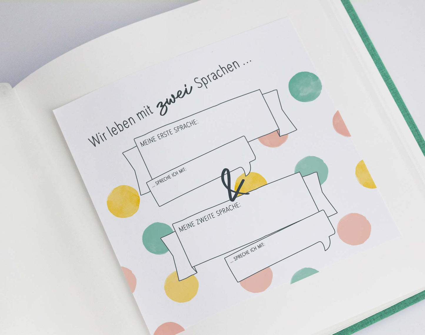Das Bild zeigt eine beispielhafte Seite aus dem Downloadset "Zweisprachigkeit". Die Seite klebt in einem klassischen Fotoalbum und hat den Titel "Wir leben mit zwei Sprachen".