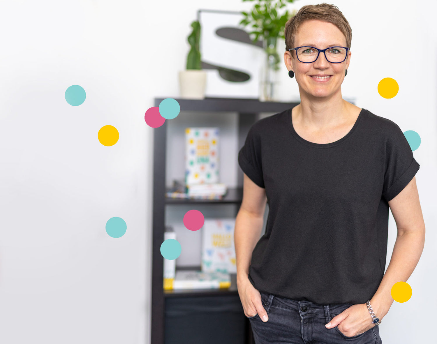 Erinnerungsbuch Autorin Katja Groborsch vor einem Regal voller HerzSeiten Bücher. Sie trägt ein schwarzes T-Shirt und schaut mit freundlichem Lächeln in die Kamera.