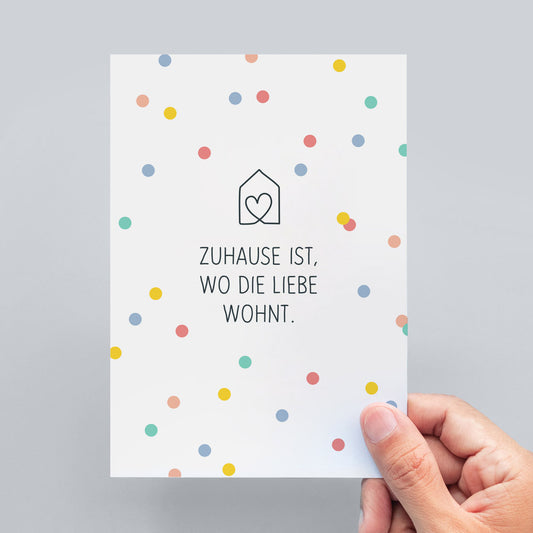 schlichte Spruch-Postkarte "Zuhause ist, wo die Liebe wohnt" mit pastellfarbigem Konfetti