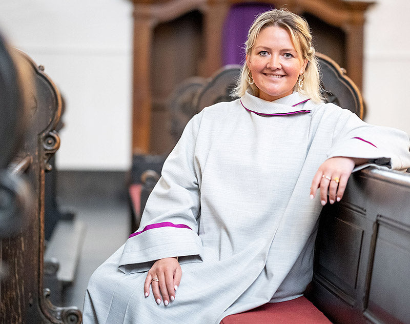 Portrait von Theologin Michelle Engel im liturgischen Gewand. Sie sitzt in einer Bankreihe der Dio-Kirche in Krefeld