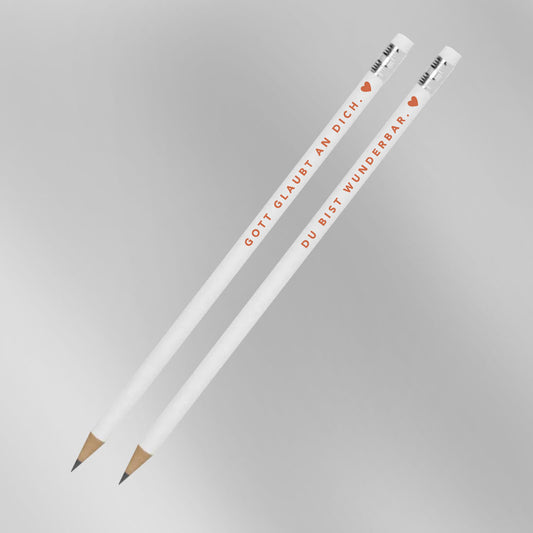 Zwei weiße Bleistifte mit Aufdruck „Gott glaubt an dich. ♥" und „Du bist wunderbar. ♥" vor grauem Hintergrund – 2er-Set christliche Bleistifte aus der himmlisch-Kollektion von herzseiten.com.