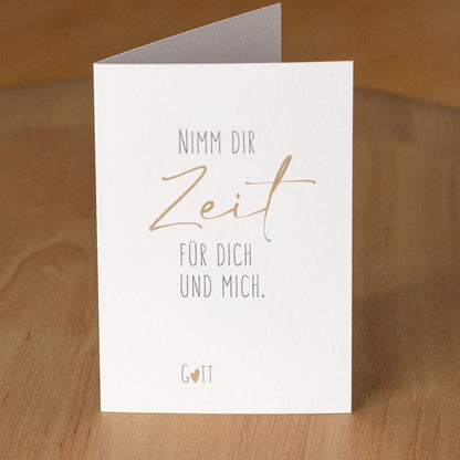 Christliche Klappkarte „Nimm dir Zeit für dich und mich. Gott" aufgestellt auf warmem Holzuntergrund – aus der „Nimm dir Zeit"-Serie von herzseiten.com.