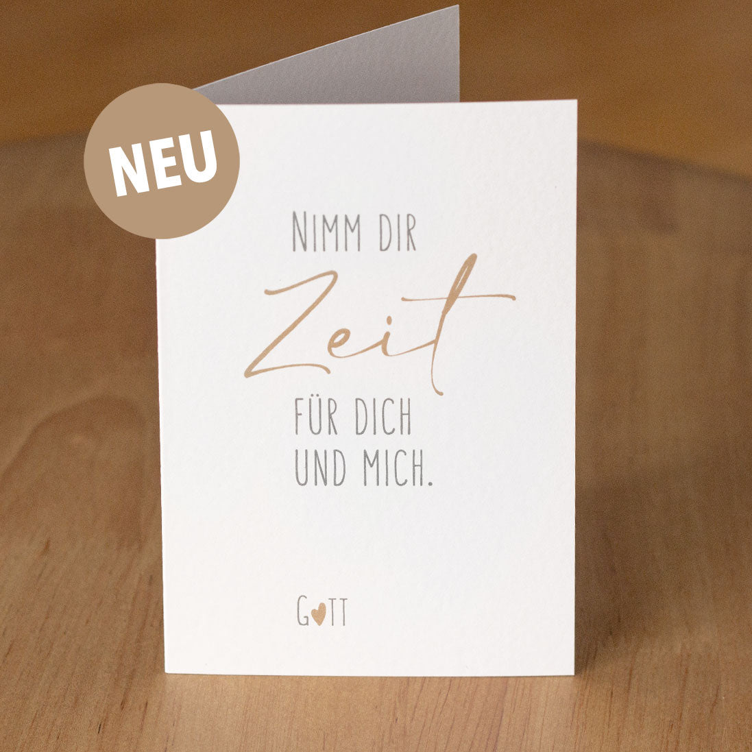 Christliche Klappkarte „Nimm dir Zeit für dich und mich. Gott" aufgestellt auf warmem Holzuntergrund – aus der „Nimm dir Zeit"-Serie von herzseiten.com.