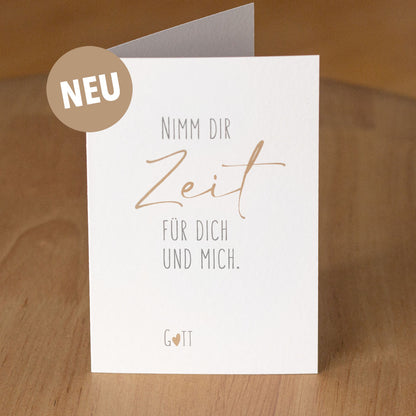 Christliche Klappkarte „Nimm dir Zeit für dich und mich. Gott" aufgestellt auf warmem Holzuntergrund – aus der „Nimm dir Zeit"-Serie von herzseiten.com.