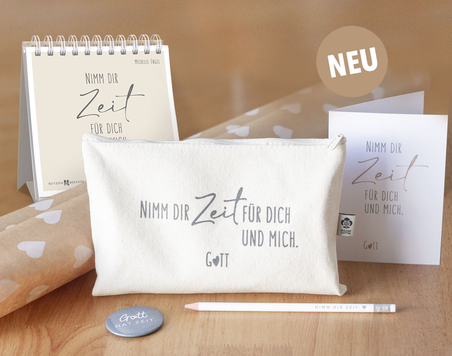 Kollektionsbild „Nimm dir Zeit für dich und mich. Gott" – alle neuen Produkte im Überblick: aufgestelltes Spiralbuch von Michelle Engel (Butzon & Bercker), naturfarbenes Baumwolltäschchen mit Organic Cotton Label, Klappkarte, weißer Bleistift „Nimm dir Zeit." und grauer Magnetbutton „Gott hat Zeit." auf Holzuntergrund mit Kraftpapier – neue himmlisch-Kollektion von herzseiten.com.