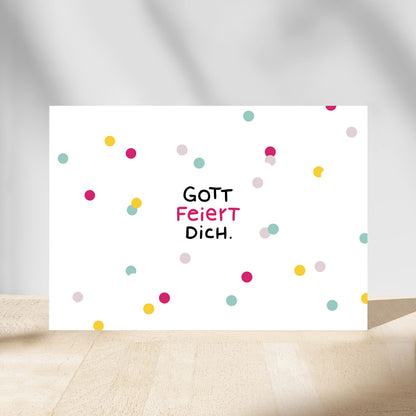 Christliche Postkarte „Gott feiert dich." mit bunten Konfetti-Punkten in Pink, Türkis, Gelb und Rosé auf weißem Hintergrund – perfekt zu Geburtstag oder Kommunion