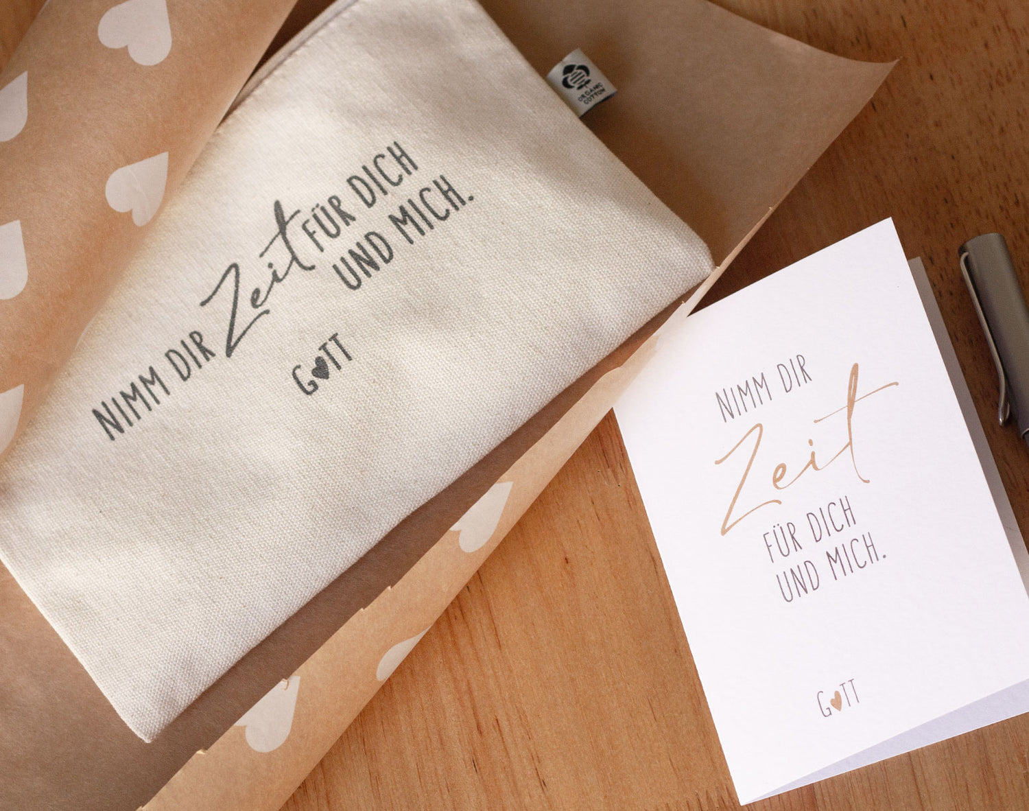 Naturfarbenes Baumwolltäschchen „Nimm dir Zeit für dich und mich. Gott" mit passender Klappkarte, auf Kraftpapier mit Herzmuster – christliche Geschenkidee aus der „Nimm dir Zeit"-Serie von herzseiten.com.